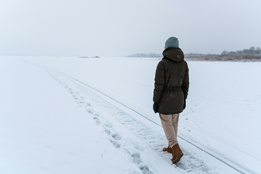 Woman walking alone in misty winter field. Solitude concept