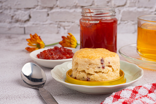 Scones traditional English delicious freshly baked homemade, strawberry jam on a wooden tray with a cloth and a teacup with a white brick wall. Dessert, beverage, and relaxation concept.