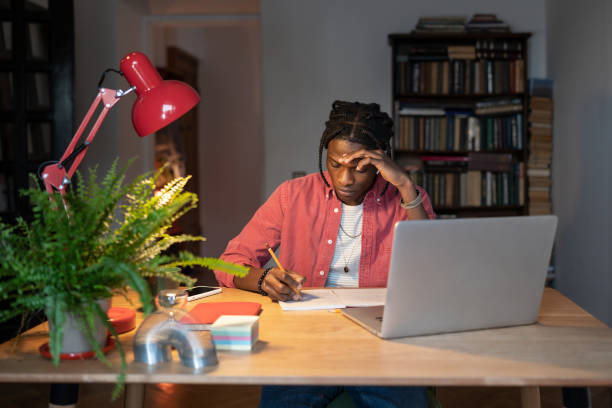 istock Hardworking young African guy student writing notes while watching webinar on laptop at home 1445117791