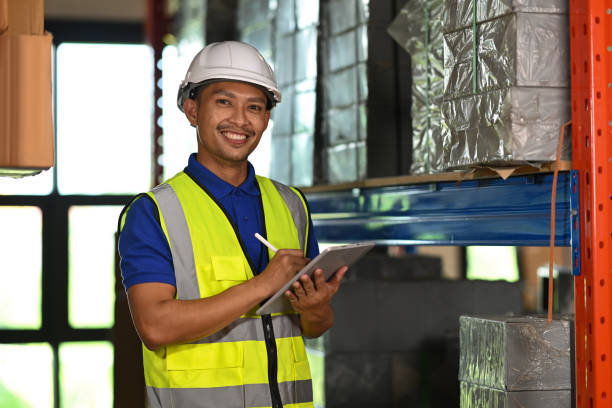 istock Handsome warehouse worker wearing security vest using digital tablet while standing near the stack of cardboard boxes. 1445119528