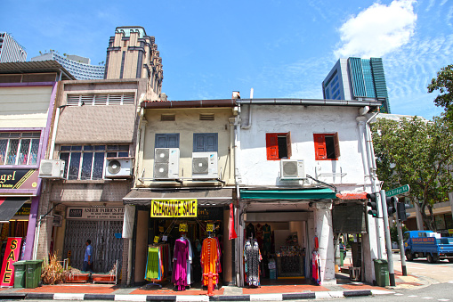 Old shop houses in Arab Street in the Arab Quarter of Singapore selling colourful clothing. Tall modern buildings can be seen in the background.