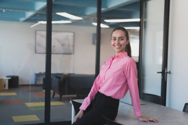 retrato da jovem mulher de negócios sorridente no escritório criativo da startup de coworking em espaço aberto. empresária de sucesso no cargo com copyspace. colegas de trabalho trabalhando em segundo plano. - real people young women women beautiful - fotografias e filmes do acervo