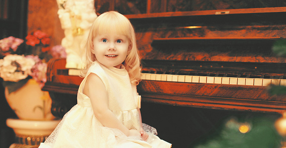 Portrait of happy smiling little girl child playing on piano at home near christmas tree