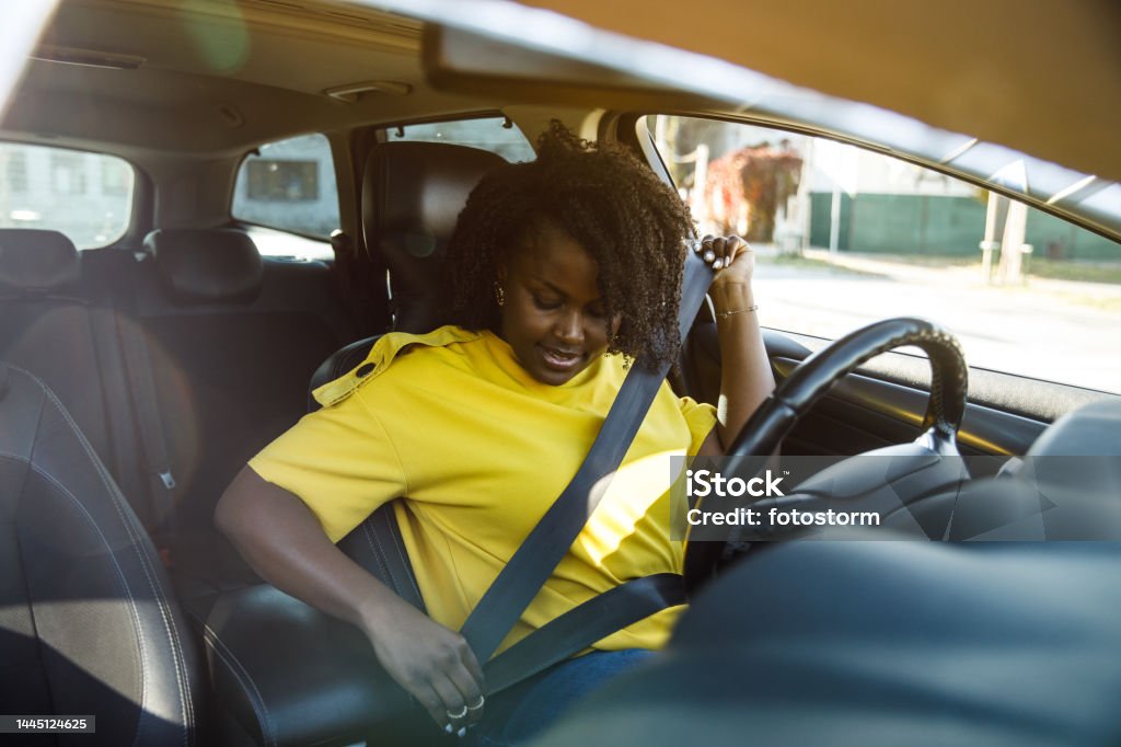 Responsible young woman sitting in her car and fastening a seat belt before she starts driving Copy space shot of smiling young woman sitting in driver's seat in her car and fastening her seat belt before she starts driving. Seat Belt Stock Photo