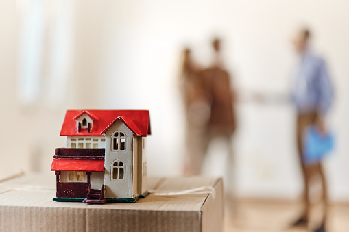 Close up of a model house on cardboard box with people in the background. Copy space.