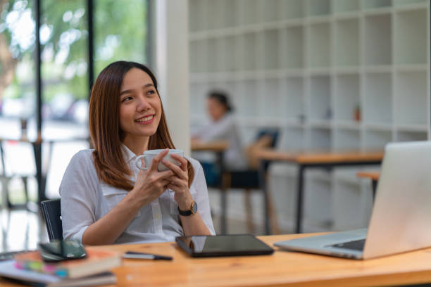 istock Beautiful woman holding a coffee cup and using a laptop while sitting at her working place in an office. 1445128530
