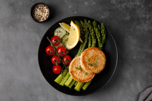 chuletas de pescado o chuletas de pollo, empanadas con espárragos hervidos y tomates cereza, idea de cena. dieta cetogénica. vista superior. - fish cutlet fotografías e imágenes de stock