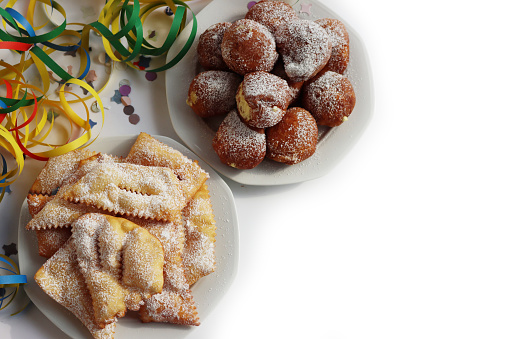 Traditional italian Crostoli ( also called chiacchere, frappe, bugie, cenci, galani) and fritters called Frittelle with cream on white background with Confetti and coloful Carnival decorations