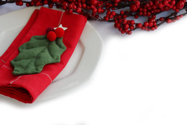 Festive table setting for Christmas with red berries decoration, White ceramic plate. Holly leaves and red tablecloth on a white background