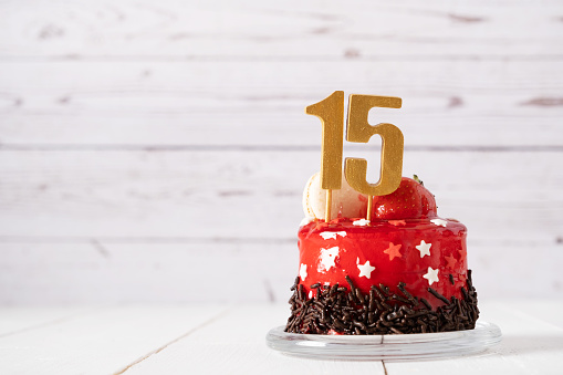 The number Fifteen on a red birthday cake on a light background.