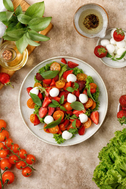istock Dinner diet Dish, fresh salad with cherry tomatoes, strawberry, mozzarella cheese, basil on beige background. Healthy lunch, bright salat. 1445132934