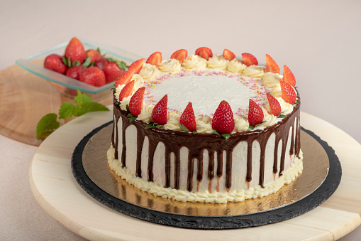 Strawberry cake with cheese cream and pieces of strawberries on a slate tray and a wooden board. There is bowl with strawberries on the background.