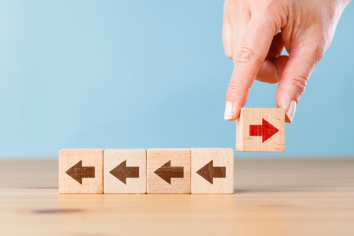 Woman hand holding block with red arrow facing the opposite direction other arrows. Think different, standing out from the crowd