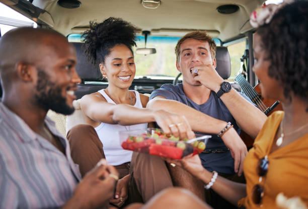 Diversity, food and friends on road trip with fruit while on holiday vacation eating watermelon, grapes and strawberry. Happy and hungry young men and women enjoying healthy fresh organic produce Diversity, fruit and friends on caravan road trip fruit while on holiday vacation eating watermelon, grapes and strawberry. Happy and hungry young men and women enjoying healthy fresh organic produce black man eating watermelon stock pictures, royalty-free photos & images