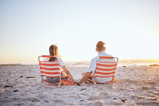 Love, couple and holding hands while on beach together enjoy sunset, ocean and relax while on sand, holiday and vacation. Romance, man and woman have fun seaside getaway for anniversary and date.