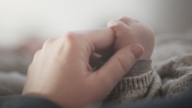 Close-Up Of A Mother Holding And Gently Stroking The Hand Of Her Newborn Child - Parenthood, Childhood, Care, Love, Trust