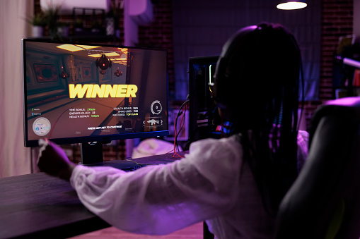Content creator playing video games tournament on computer, celebrating win. Female player winning action gaming championship, having fun with online gameplay competition on pc.
