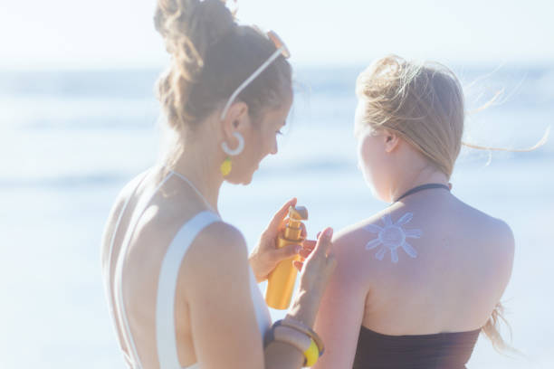 современная мама и дочь-подросток на пляже с использованием солнцезащитного крема - teenager parent beach contemporary стоковые фото и изображения