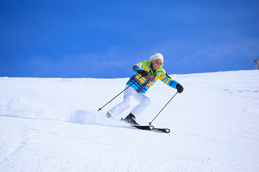 Vital senior, gray-haired men snow skier skiing, enjoying on sunny ski resorts. Skiing carving at high speed against blue sky.