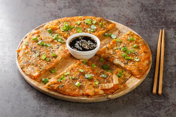 Kimchijeon is a Korean savory crispy pancake made of kimchi with flour and onion closeup on the wooden board on the table. Horizontal