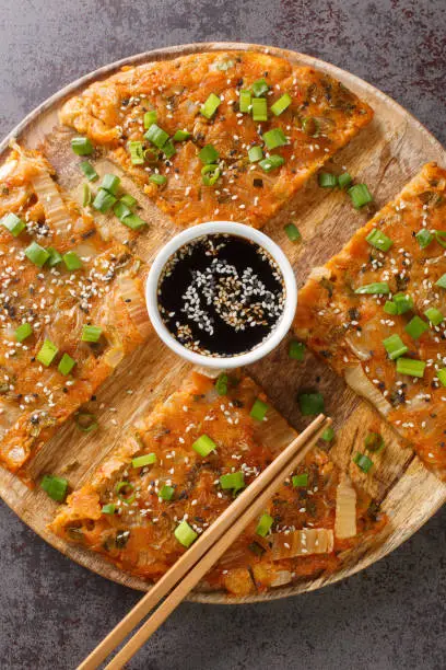 Korean Pancakes Kimchijeon is basically made with kimchi and a little scallions closeup on the wooden board on the table. Vertical top view from above