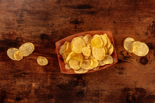 Potato chips or crisps in a bowl, shot from above on a wooden background with copy space