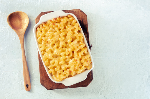 Macaroni and cheese pasta in a casserole, overhead flat lay shot with a wooden spoon and copy space