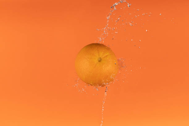 An orange in the air with a beautiful water splash