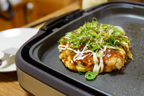 okonomiyaki giapponese sulla piastra calda - okonomiyaki foto e immagini stock