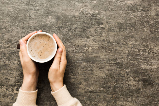 Minimalistic style woman hand holding a cup of coffee on Colored background. Flat lay, top view cappuccino cup. Empty place for text, copy space. Coffee addiction. Top view, flat lay stock photo