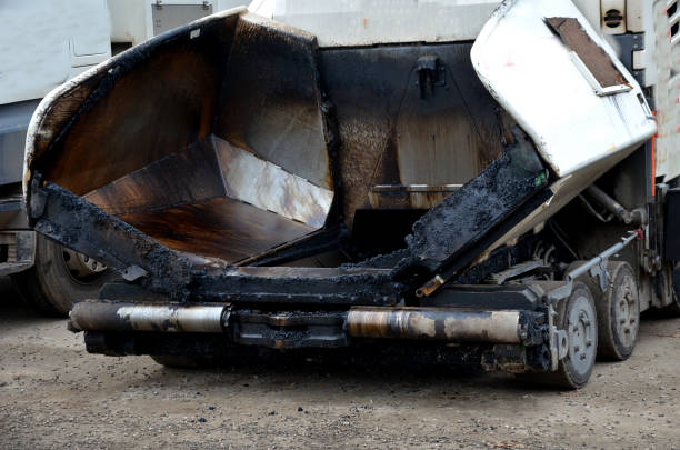 istock Asphalting work using heaters and dosing pavers. Asphalt spills a truck with a body. smaller cylinders compress the pavement surface. a park is being created by the water 1445162060