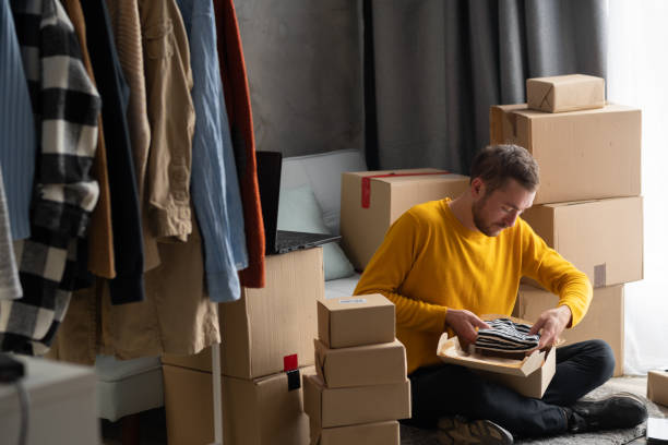 junger mann start-up-kleinunternehmer packstoff in der box zu hause, freiberuflicher verkäufer bereitet produkt für verpackungsprozess im online-shop vor. kleinbetrieb - small business office business unpacking stock-fotos und bilder