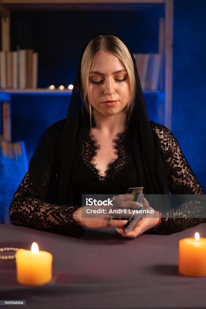 Woman fortune teller chooses a deck of cards for divination in smoke with candles Woman fortune teller chooses a deck of cards for divination in smoke with candles. Copy space One Woman Only Stock Photo