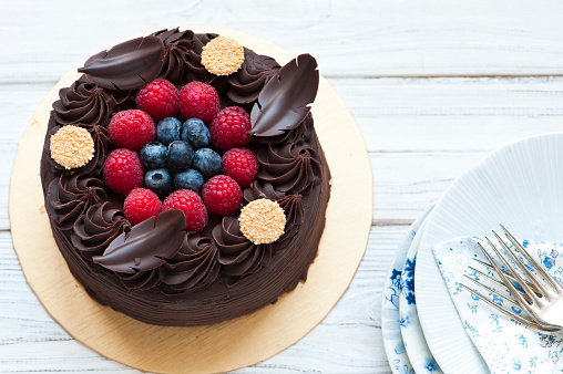 Chocolate cake with berries. The delicious cake sits on a white table with plates and forks. Christmas chocolate cake.