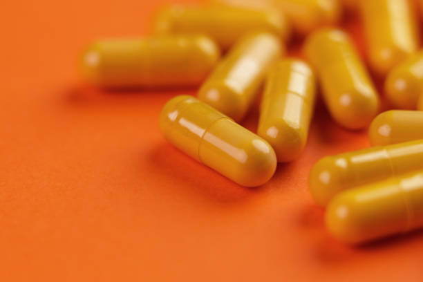 주황색 배경에 있는 노란색 제약 의료 캡슐 - vibrant color healthcare and medicine healthy lifestyle vitamin pill 뉴스 사진 이미지