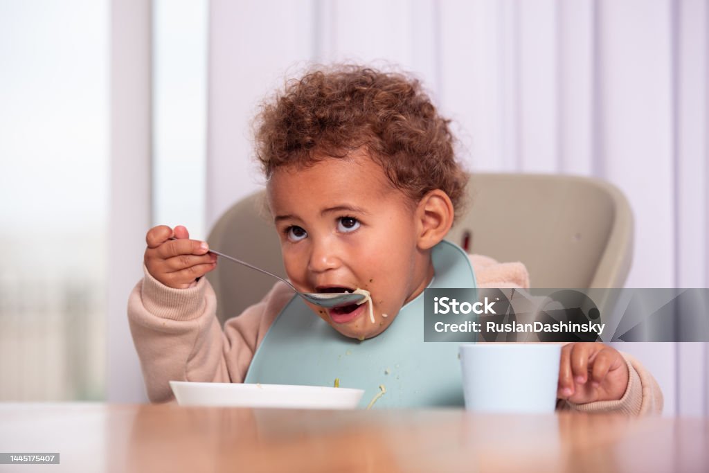 Baby girl eating from a plate. Baby girl eating from a plate, sitting on a high chair. Spoon Stock Photo