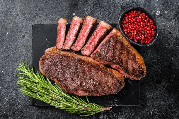 Grilled top sirloin or cup rump beef meat steak on marble board. Black background. Top view.