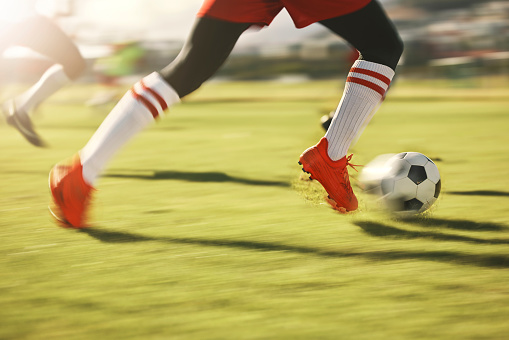 Soccer, sports and running with the shoes of a man athlete on a grass pitch or field during a game. Football, fitness and training with a male player dribbling during a match or cardio workout