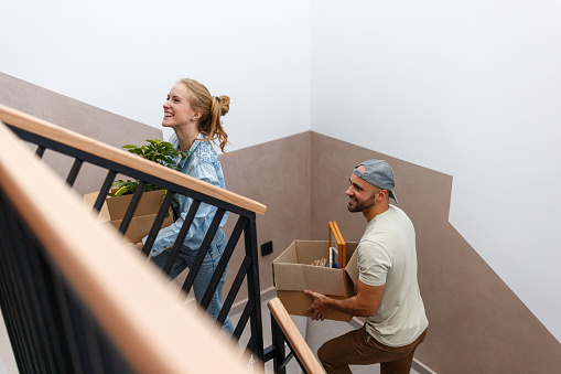 Happy couple climbing up the stairs while carrying a boxes into their new apartment
