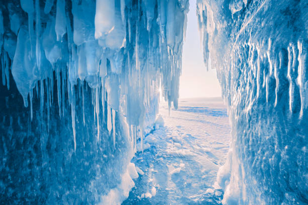 Ice cave with icicles on Baikal lake at sunset. Blue ice in the evening sunlight. Winter landscape of Baikal lake, Siberia, Russia