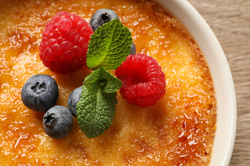 Delicious creme brulee with fresh berries on wooden table, closeup