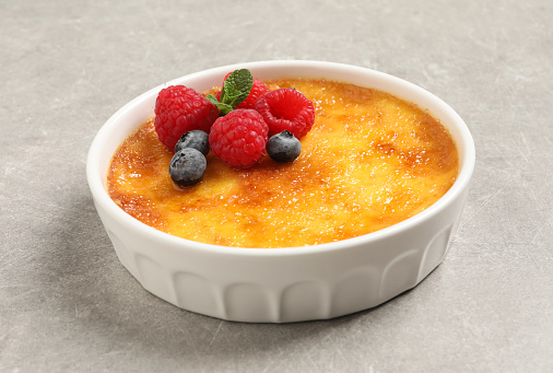 Delicious creme brulee with fresh berries on light grey table, closeup