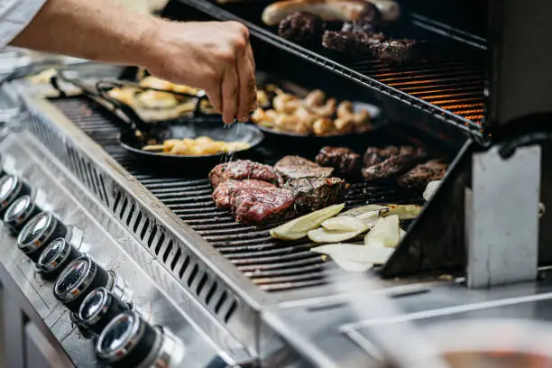 Photo of Human hand adds salt to the steaks on the barbecue