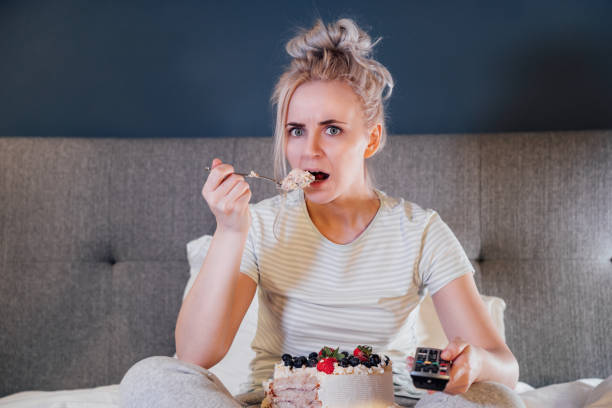 istock Emotionally stressed, shocked woman eating cake and holding a remote control while watching TV in bed. Scary horror movie or terrible news, scare in her eyes Overeating, Jamming of negative emotions. 1445185674