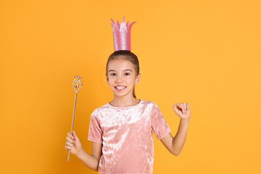 Cute girl in pink crown with magic wand on yellow background. Little princess