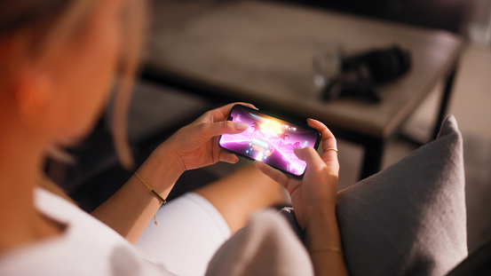 Woman playing a mobile game on her smartphone. She is in her apartment living room by herself.