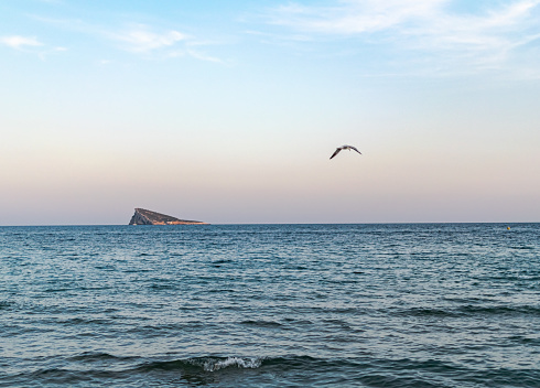 Benidorm, Alicante, Valencia, Spain. Colorful blue sky with clouds, red and orange colors in the horizon line at sunset golden hour with a sailboat moored near the island.