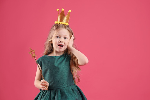 Cute girl in fairy dress with golden crown and magic wand on pink background, space for text. Little princess