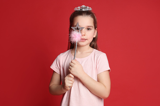 Cute girl in diadem with magic wand on red background. Little princess