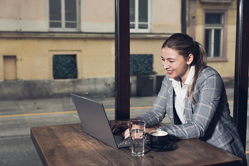 Young business woman sitting in the coffee shop during the lunch break drinking coffee and work on the laptop computer. Freelancer business person working on the new project for foreign company.